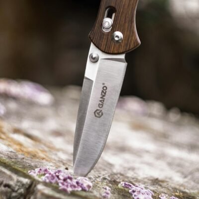 Close-up image of a Ganzo knife embedded in wood, highlighting its sharpness and steel texture.