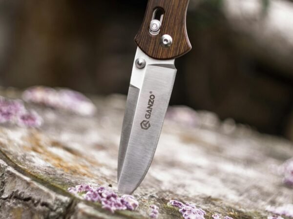 Close-up image of a Ganzo knife embedded in wood, highlighting its sharpness and steel texture.